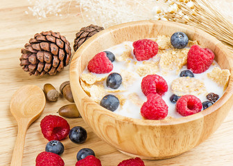 Bowl of cereals with raspberries and blueberrys on a wooden table.