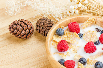 Bowl of cereals with raspberries and blueberrys on a wooden table.