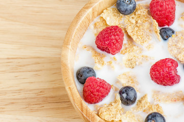 Bowl of cereals with raspberries and blueberrys on a wooden table.