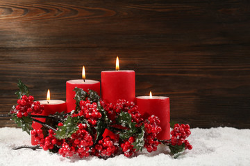 Red candles and branch of holly berries in a snow over wooden background, still life
