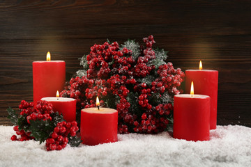 Candles and branch of holly berries in a snow over wooden background, still life