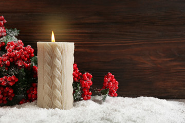 Candle and branch of holly berries in a snow over wooden background, still life