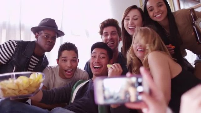 Group of friends having a party taking a photo with a smartphone laughing and smiling together