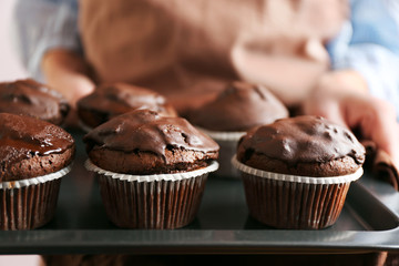 Housewife holding oven-tray with chocolate cupcakes, close up