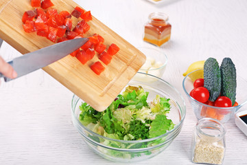 Female hands adding pieces of salmon into bowl with salad, close-up