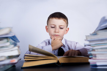 Little child thinking leaning on pile of books, isolated grey background.Thoughtfully child with a stack of books leaning on them.Education concept