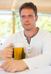 Handsome man with beer in summer cafe.