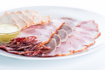 Assorted meat: ham, smoked sausage, salami, chicken, tongue and mustard on a white background