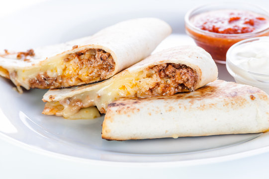 Mexican quesadilla with meat and cheese, hot sauce and cream on a white background
