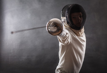 Boy wearing white fencing costume and black fencing mask standing with the sword practicing in fencing.  - obrazy, fototapety, plakaty