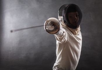 Boy wearing white fencing costume and black fencing mask standing with the sword practicing in fencing. 