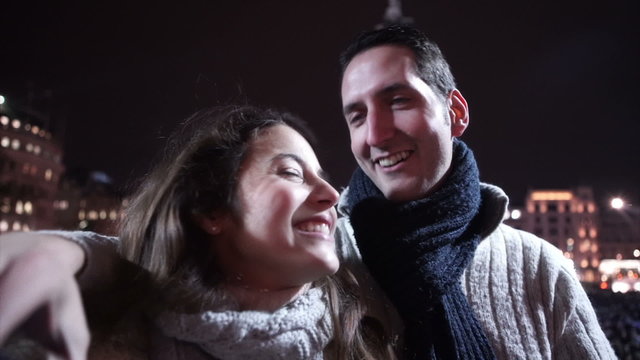 Romantic kissing couple take a selfie with city centre xmas tree in background. Shot on RED Epic.