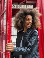 Naklejka premium Smiling portrait of young woman close to red telephone box in London.