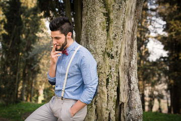 Smiling hipster young man relaxing smoking a cigarette outdoors