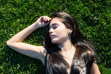 Young woman relaxing in Central Park laying on the grass and listening to music.