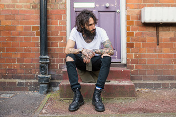Intense portrait of young tattooed man sit on the street in Shoreditch. London.