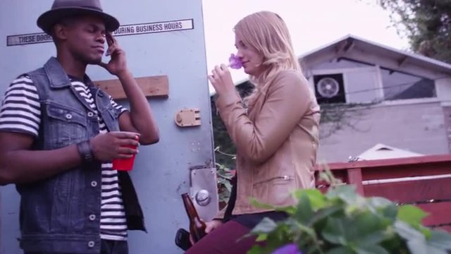 Cute young black and caucasian hipster couple talking in doorway ay party drinking and smiling