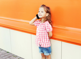Happy smiling little girl child talking on smartphone in city