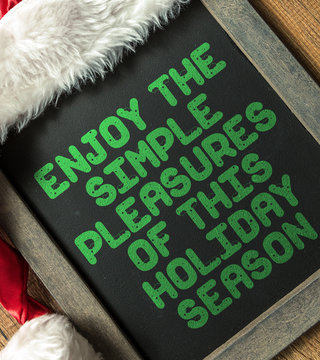 Enjoy the Simple Pleasures Of This Holiday Season written on blackboard with santa hat