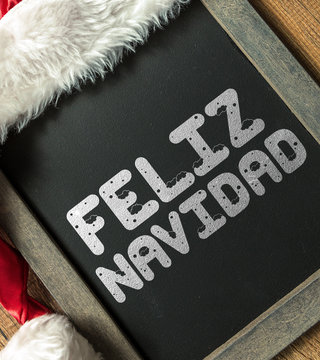 Merry Christmas (in Spanish) written on blackboard with santa hat