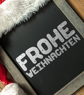 Merry Christmas (in German) written on blackboard with santa hat