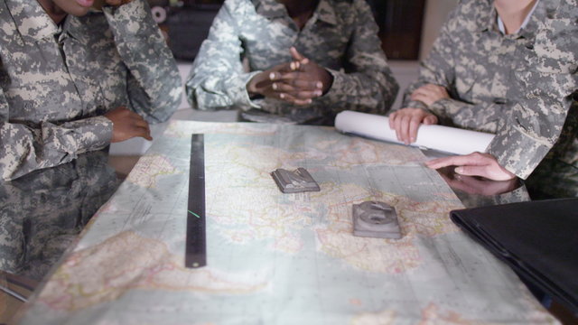 Female military officers in army office, looking at a map and discussing battle strategy. 