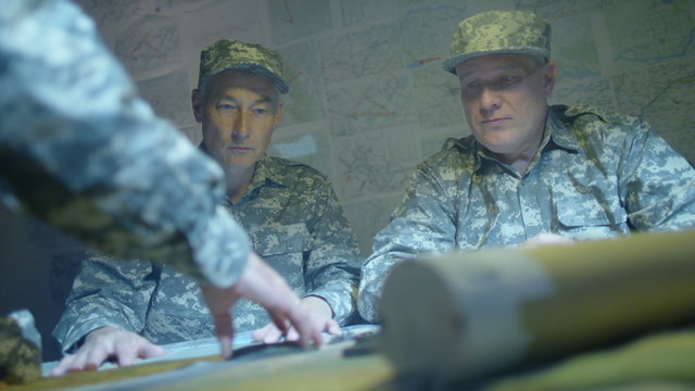  Military officers in army bunker, looking at map & discussing battle strategy