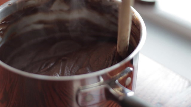 Closeup of a woman stirring steaming melted chocolate in a metal pot with a wooden spoon