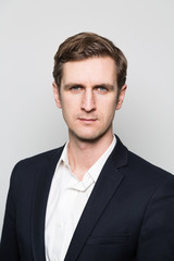 Blond-haired european businessman with a stern look stares into the camera while in front of a gradient background