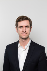 Portrait of blond-haired businessman in front of a gradient wall looking at the camera 