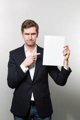 Blond-haired european businessman shows something on a piece of paper with squeezed eyes while in front of a gradient background