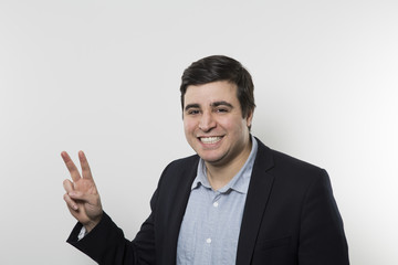 Dark-haired European businessman giving the peace sign and smiling. Studio shot.  