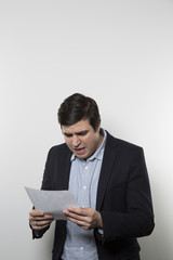 Dark-haired european businessman with a vine look stares at a piece of paper while in front of a gradient background