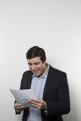 Dark-haired european businessman with a happy look and a good laugh stares at a piece of paper while in front of a gradient background