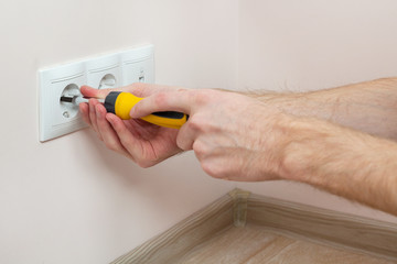 The hands of an electrician installing a wall power socket