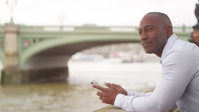  Attractive man on his own in London using mobile phone by the side of the River Thames. 