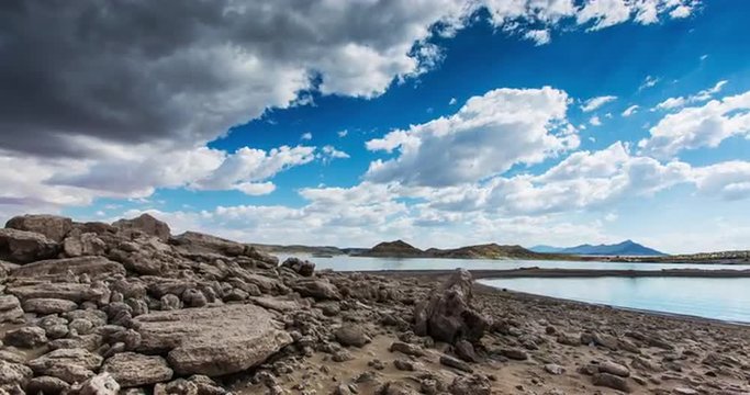 Rocky Beach Time Lapse Shore. a time lapse moves right on a rocky beach shore line from a pile of rocks. Clouds fly over top the lake.
