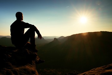 Hiker take relaxing on a rock and enjoying sunset at horizon. Vivid effect.