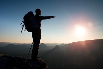 Sharp silhouette of a tall man on the top of the mountain with sun in the frame. Tourist guide in...