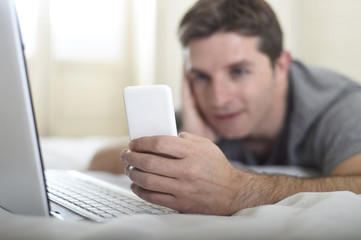 young attractive man lying on bed or couch using mobile phone and computer laptop internet addict