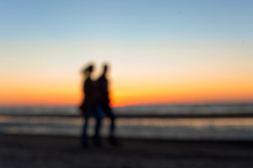Fototapeta na wymiar Two people defocused silhouettes walking along the beach on suns