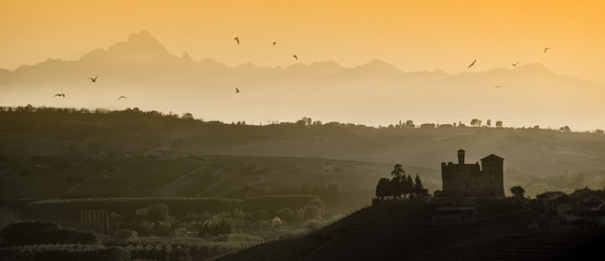 View the sunset over the hills of the Castle of Grinzane Cavour Unesco heritage in the territory of the Langhe Piedmont Italy, migratory birds flying in the sky