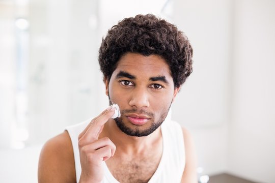 Serious man putting shaving foam on his face