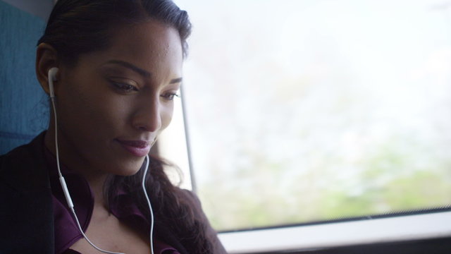  Beautiful woman on train journey relaxing with earphones and computer tablet.
