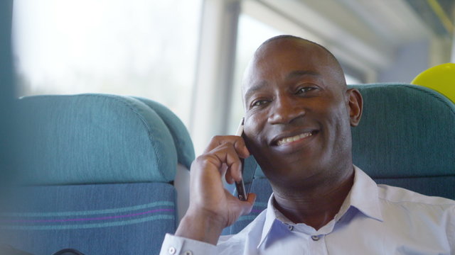 Smiling businessman making mobile phone call on train journey.