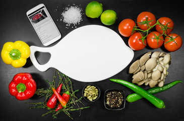 Phone and white cutting board among the vegetables. Top view 