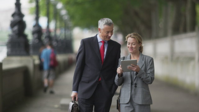 Businesspeople walking, talking and looking at data on tablet and smiling