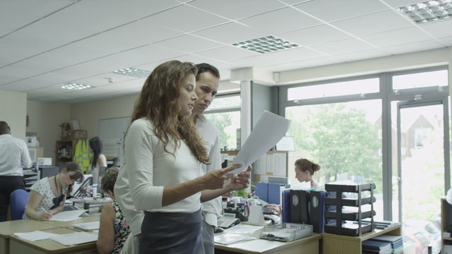  Managerial team walking through busy small business offices. Employees at work in modern building. Workers on computers. Casual business people discussing projects in product manufacturing company.