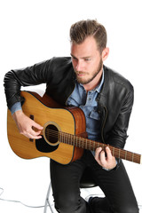 Obraz premium A man wearing a black leather jacket sitting down with an acoustic guitar. White background.
