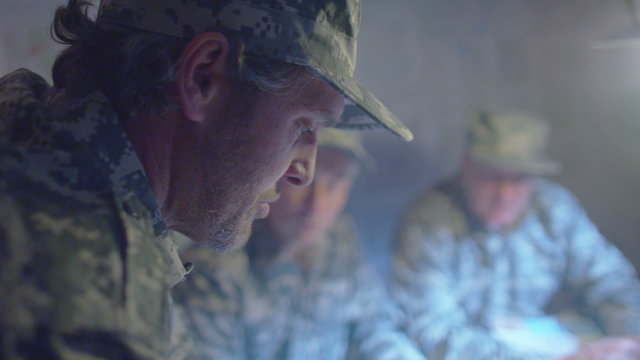  Military officers in army bunker, looking at map & discussing battle strategy
